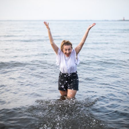 Młoda kobieta stoi po kolana w morzu i chlapie w stronę kamery