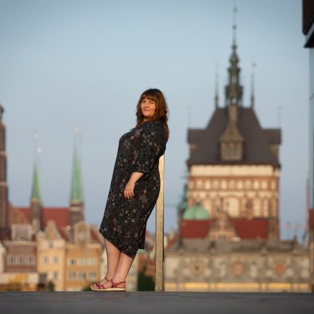 Młoda kobieta w sukience stoi na tle gdańskich budowli