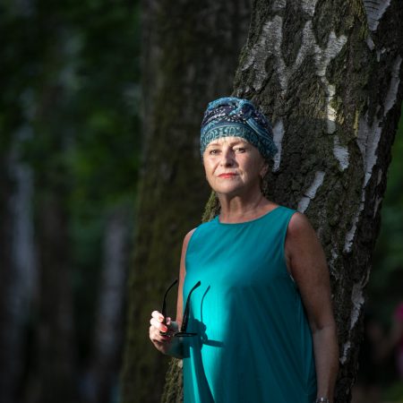 Starsza kobieta w zielonym turbanie i zielonej sukience na tle drzewa