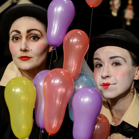 Dwie aktorki w melonikach wśród kolorowych balonów