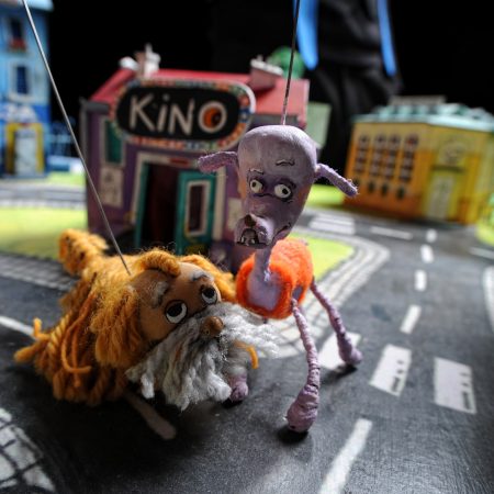 Dwie lalki psów na makiecie miasteczka przed budynkiem z napisem Kino